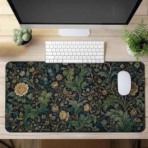 May include: A rectangular desk mat featuring a dark navy blue background with an intricate pattern of cream-coloured flowers, blue bell-shaped blossoms, and lush green acanthus leaves. The mat is positioned on a light wood surface under a computer.