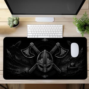 May include: A rectangular black desk mat featuring a central graphic of a Viking helmet positioned in front of two crossed battle axes. The background displays a dark landscape with a Viking longship on water, a flying raven, and circular runic patterns.