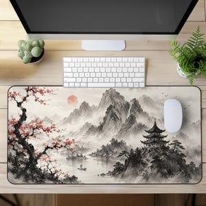 May include: A rectangular desk mat featuring a landscape illustration with a cherry blossom tree on the left, a pagoda on a rocky cliff to the right, a small boat on the water, and distant mountains under a pale red sun in a soft ink wash style.