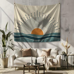 Pu&ograve; includere: Un arazzo beige con un design minimalista raffigurante un sole arancione sopra onde turchesi. I raggi del sole sono rappresentati da linee blu scuro. L'arazzo &egrave; appeso sopra un divano bianco in un soggiorno.
