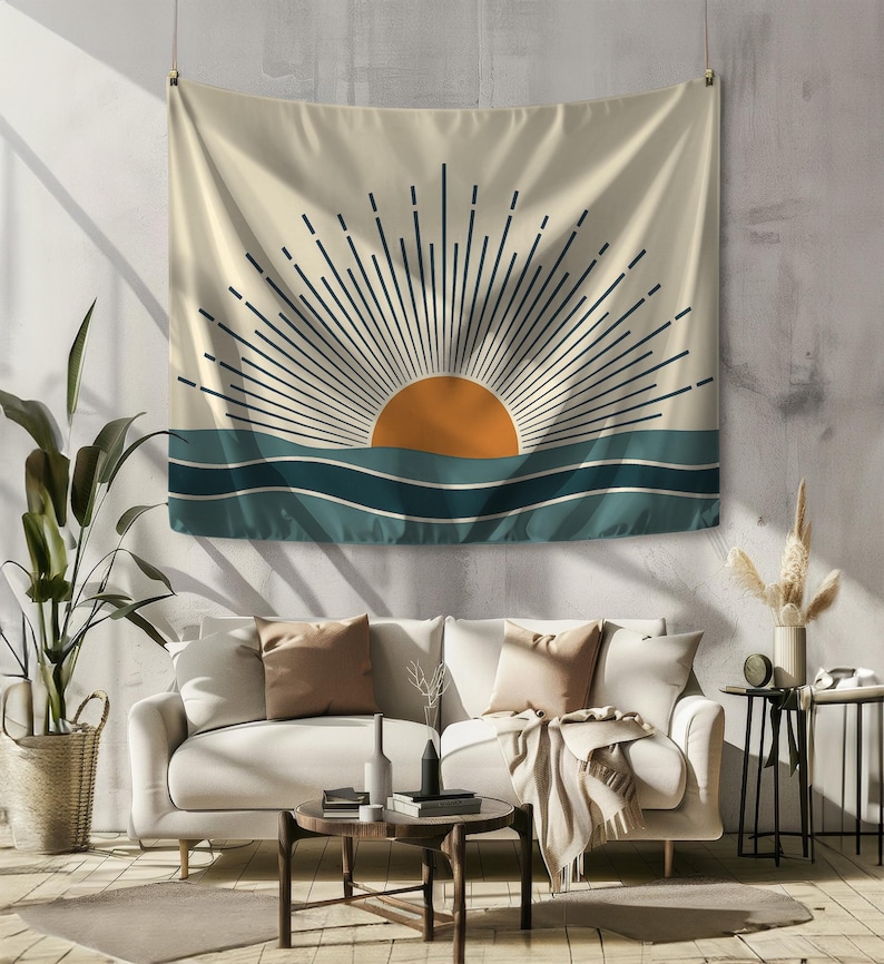 Pu&ograve; includere: Un arazzo beige con un design minimalista raffigurante un sole arancione sopra onde turchesi. I raggi del sole sono rappresentati da linee blu scuro. L'arazzo &egrave; appeso sopra un divano bianco in un soggiorno.