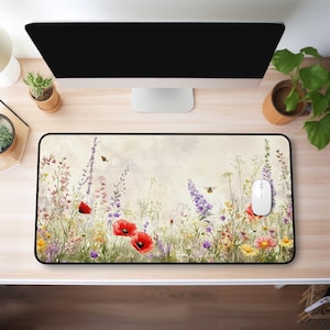 May include: A rectangular mouse mat with a watercolour painting of a wildflower meadow. The design includes red poppies, purple lavender, yellow daisies, and butterflies. A white computer mouse is on the right side of the mat.