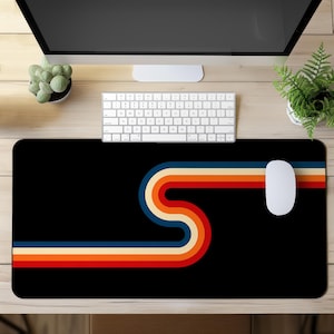 Peut inclure: Un tapis de bureau rectangulaire noir orné d'un motif graphique horizontal composé de bandes parallèles bleu marine, crème, orange et rouge. Les bandes forment une courbe en S au centre du tapis, offrant une surface lisse pour une souris.