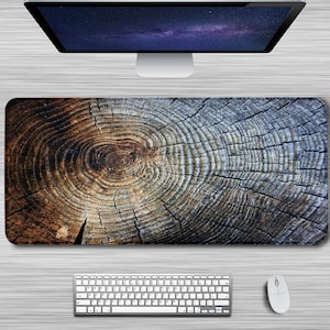 May include: A brown and grey wooden desk mat with a tree ring pattern. The mat is on a white desk with a computer monitor, keyboard and mouse.