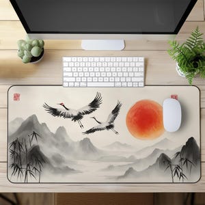 Op de afbeelding: Rechthoekige muismat met een serene landschap. Twee kranen vliegen over mistige bergen, een grote oranje zon en bamboe. Gedempte kleurenpalet. Een witte muis en toetsenbord liggen op het bureau.