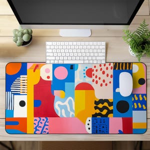 Op de afbeelding: Een muismat met een kleurrijk abstract ontwerp met geometrische vormen en patronen in tinten rood, geel, blauw, roze, zwart en wit.