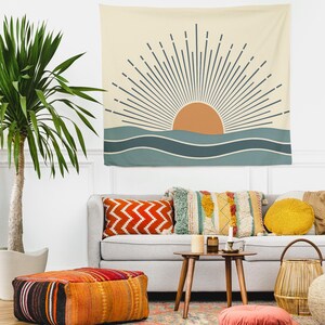 Pu&ograve; includere: Un arazzo da parete beige con un design a sole e oceano. Il sole &egrave; arancione, con raggi blu scuro. L'oceano &egrave; rappresentato da onde blu. L'arazzo &egrave; appeso sopra un divano grigio con cuscini colorati e un pouf fantasia.