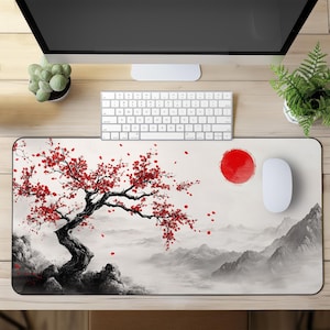 Puede incluir: Una alfombrilla de ratón blanca con un diseño de inspiración japonesa en negro y rojo. El diseño presenta un cerezo en flor con flores rojas y un sol rojo en el fondo. La alfombrilla de ratón es rectangular y tiene una superficie lisa.