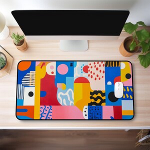 Op de afbeelding: Een muismat met een kleurrijk abstract ontwerp en een zwarte rand. Het ontwerp bevat geometrische vormen in tinten rood, geel, blauw, roze en zwart.