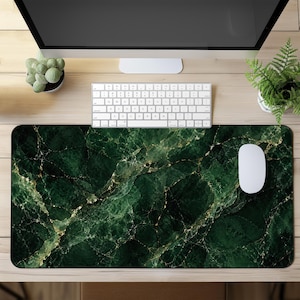 Peut inclure: Tapis de bureau rectangulaire avec un motif de marbre vert foncé et des veines dorées. Une souris et un clavier d'ordinateur blancs sont posés sur le tapis. Le tapis est sur un bureau en bois clair avec un écran d'ordinateur et des plantes.