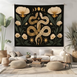 May include: Black tapestry with a botanical design. It features two intertwined snakes in gold and cream, surrounded by cream flowers and green foliage. Gold stars, moons, and a key complete the design. The tapestry is displayed in a living room setting.