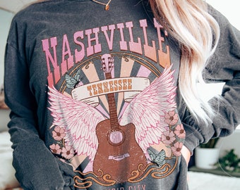 May include: A gray long-sleeve shirt with a vintage-style graphic of a guitar with wings and the text "Nashville Tennessee Music City".