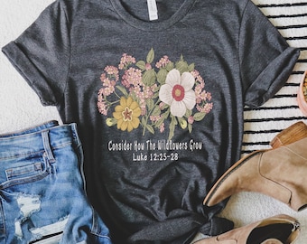 Puede incluir: Una camiseta gris oscura con un diseño floral y el texto "Consider How The Wildflowers Grow Luke 12:25-28".