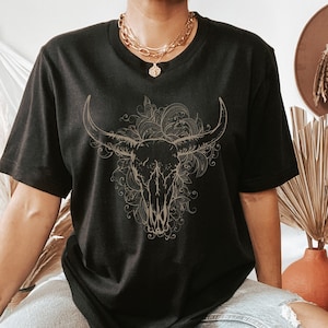 Peut inclure: T-shirt noir avec un contour dor&eacute; d'un cr&acirc;ne de taureau avec des d&eacute;tails floraux.