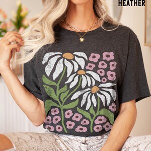 K&ouml;nnte beinhalten: Dunkelgraues T-Shirt aus Heather-Material mit einem grafischen Druck von wei&szlig;en G&auml;nsebl&uuml;mchen und rosa Blumen.