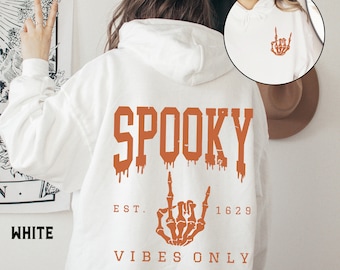 May include: White hoodie with a dripping orange "SPOOKY" graphic, a skeleton hand giving the middle finger, and the text "EST 1629 VIBES ONLY".