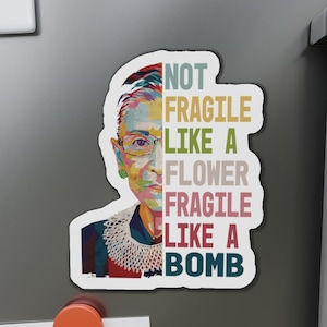 May include: A colorful illustration of Ruth Bader Ginsburg with the text "Not Fragile Like A Flower Fragile Like A Bomb" in a vintage style.