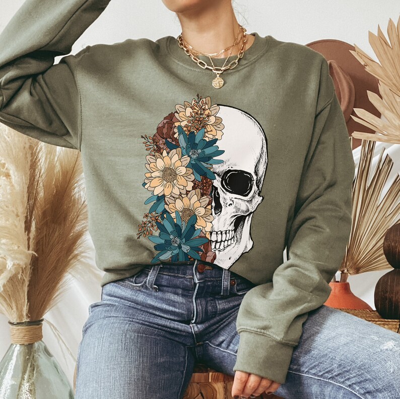 May include: A green sweatshirt with a skull and floral design. The skull is white with black eyes and a black mouth. The flowers are yellow, blue, and brown.