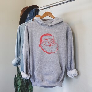 Puede incluir: Una sudadera con capucha gris con un gr&aacute;fico de Pap&aacute; Noel vintage rojo en la parte delantera.