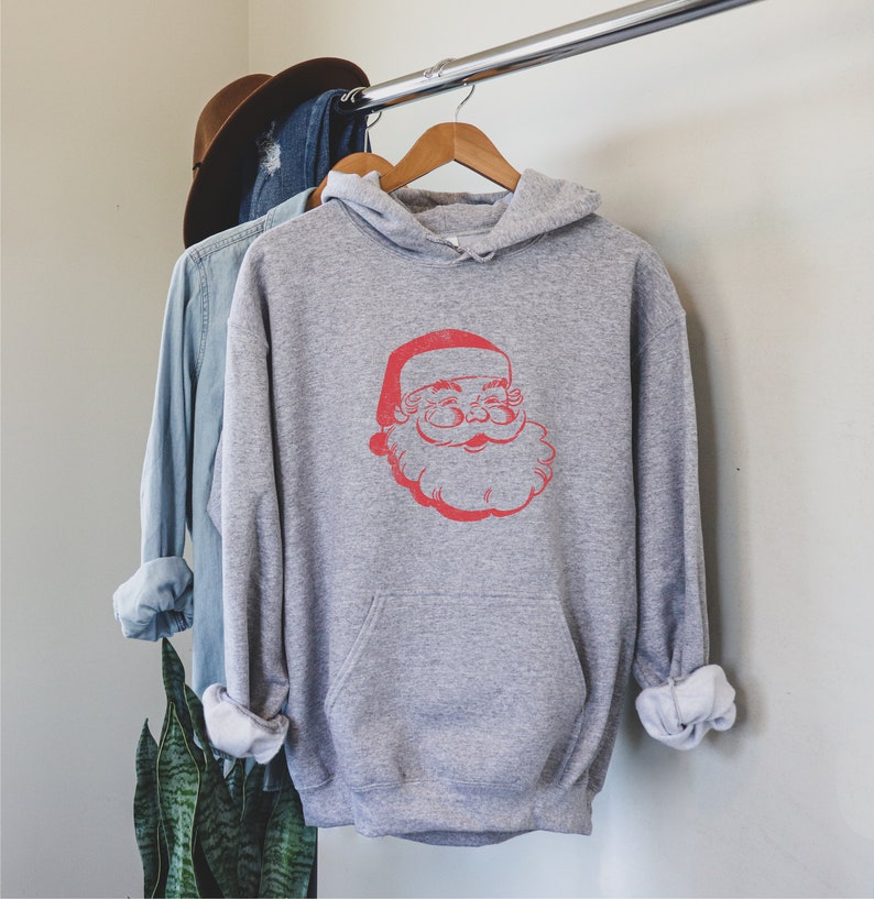Puede incluir: Una sudadera con capucha gris con un gr&aacute;fico de Pap&aacute; Noel vintage rojo en la parte delantera.