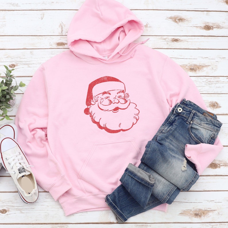 Puede incluir: Sudadera con capucha rosa con un gr&aacute;fico de Pap&aacute; Noel rojo de estilo vintage en la parte delantera.