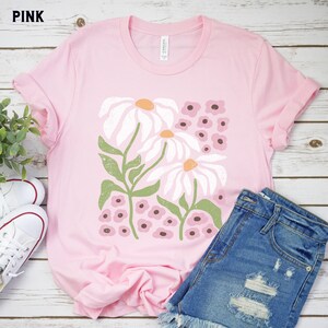 K&ouml;nnte beinhalten: Pinkes T-Shirt mit einem wei&szlig;en G&auml;nsebl&uuml;mchen-Blumendruck. Das Design zeigt wei&szlig;e G&auml;nsebl&uuml;mchen mit gr&uuml;nen Stielen und rosa und braunen Bl&uuml;tenknospen.