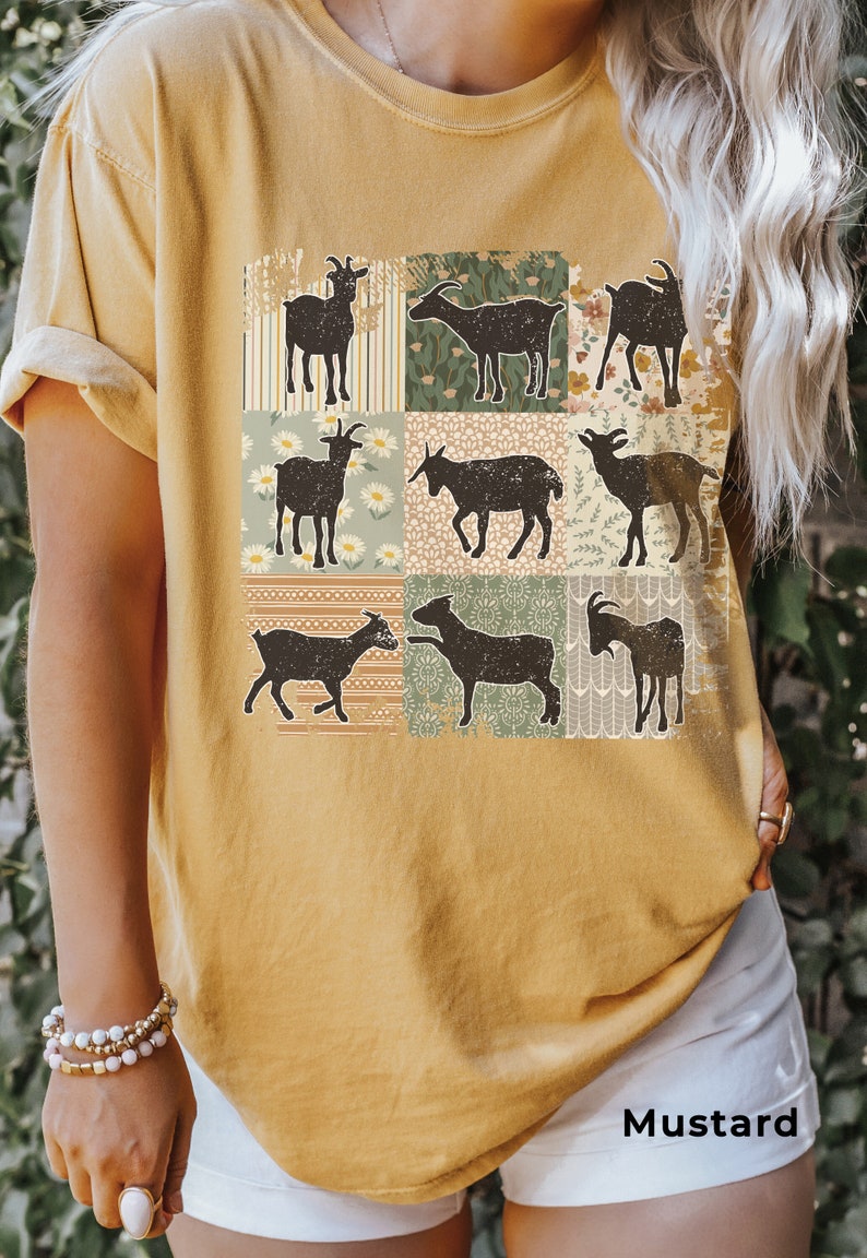 May include: A mustard yellow t-shirt with a patchwork design featuring silhouettes of goats. The design includes various floral patterns and geometric shapes.