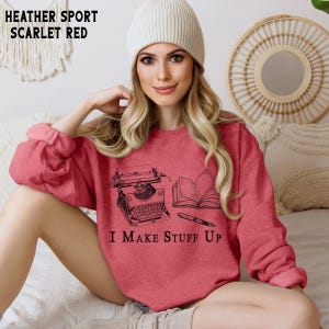 Puede incluir: Sudadera roja escarlata con un gr&aacute;fico negro de una m&aacute;quina de escribir, un libro abierto y un bol&iacute;grafo. El texto "I MAKE STUFF UP" est&aacute; impreso debajo. La sudadera es de material deportivo jaspeado.