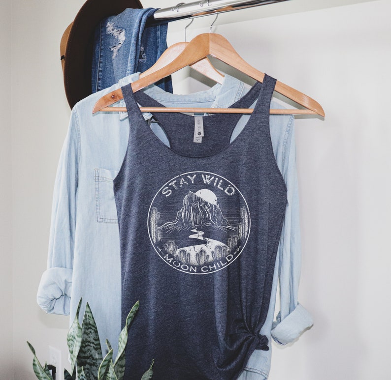 May include: A dark gray tank top with a white graphic of a mountain range and the text "Stay Wild Moon Child".
