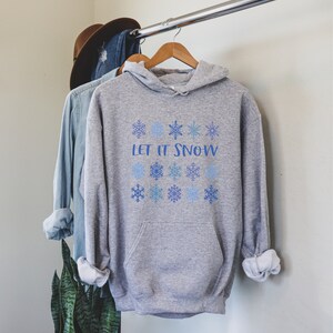 May include: A gray hooded sweatshirt with the text "Let it Snow" printed in blue. The sweatshirt is decorated with blue snowflakes.