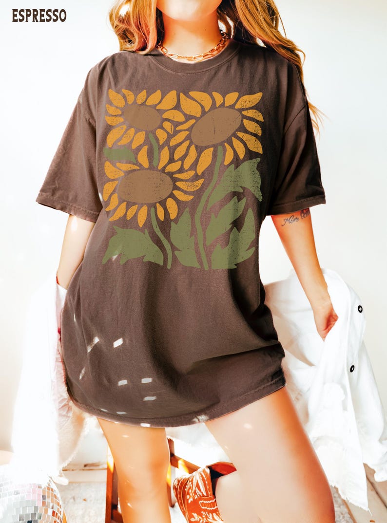 May include: A brown oversized t-shirt with a graphic print of three sunflowers in shades of yellow, orange, and brown. The sunflowers are stylized and have a vintage look.