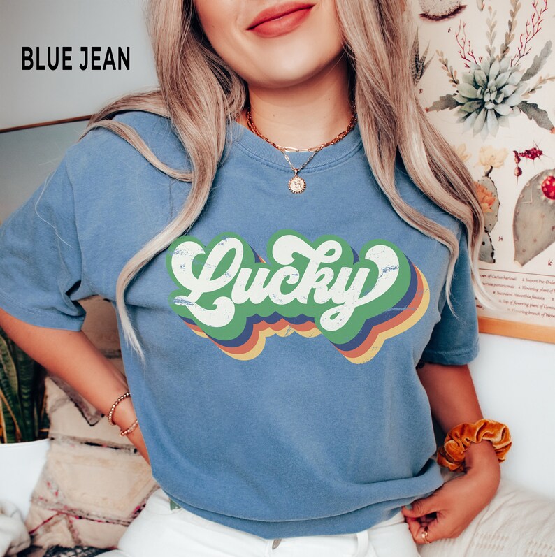 May include: A blue jean t-shirt with a retro-style graphic that says "Lucky" in rainbow colors.