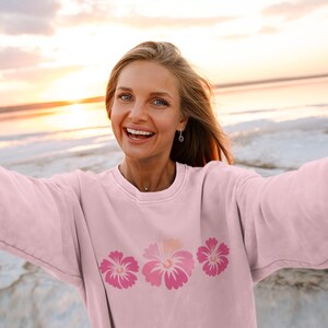 May include: A pink sweatshirt with a row of three pink hibiscus flowers printed on the front.