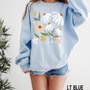K&ouml;nnte beinhalten: Ein hellblauer Pullover mit einem Blumendruck mit wei&szlig;en, rosa und gelben Blumen. Das Model tr&auml;gt Gr&ouml;&szlig;e L.