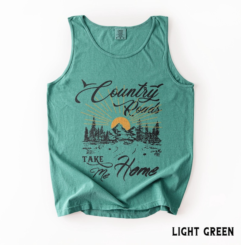 K&ouml;nnte beinhalten: Hellgr&uuml;nes Tanktop mit dem Text "Country Roads Take Me Home" in schwarzer Schrift und einer Grafik von Berg, B&auml;umen und Sonne. Das Shirt ist einfarbig und hat einen Rundhalsausschnitt.