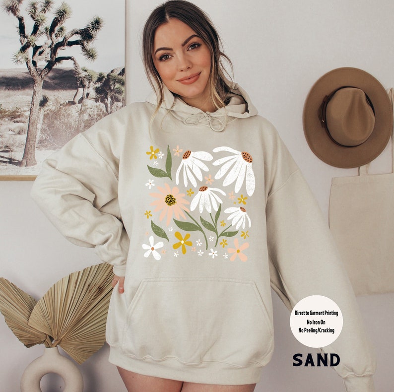 K&ouml;nnte beinhalten: Ein beiger Hoodie mit einem Blumendruck mit wei&szlig;en, rosa und gelben Blumen. Der Hoodie hat eine Kapuze mit Kordelzug und eine K&auml;ngurutasche. Der Text "Direct to Garment Printing No Iron On No Peeling/Cracking SAND" ist unten auf dem Hoodie aufgedruckt.