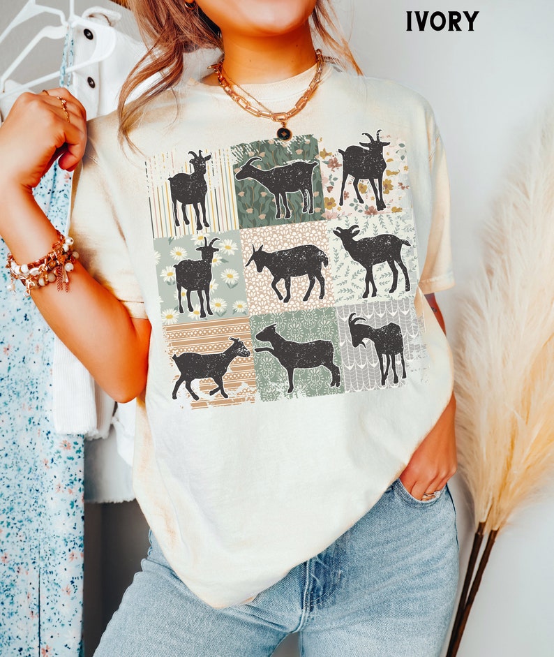 May include: A cream-colored t-shirt with a patchwork design featuring silhouettes of goats in various poses. The design is made up of squares with different patterns, including stripes, floral prints, and geometric designs.