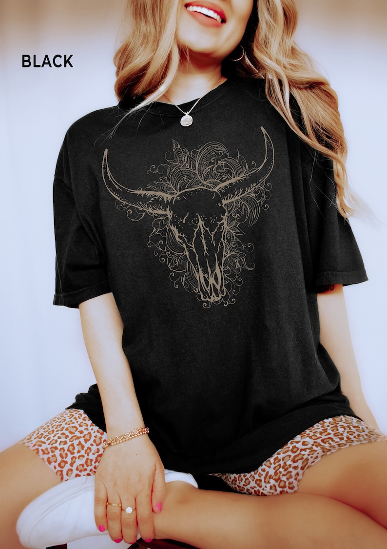 K&ouml;nnte beinhalten: Schwarzes Oversize-T-Shirt mit einem grafischen Druck eines Bullensch&auml;dels mit floralen Details. Der Text "BLACK" ist in der oberen linken Ecke des Bildes sichtbar.