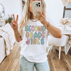 May include: White t-shirt with the text "Second Grade Vibes" in colorful letters with a peace sign graphic.