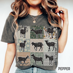 May include: A dark gray t-shirt with a patchwork design featuring nine black silhouettes of goats. Each square in the patchwork has a different floral or geometric pattern. The text "PEPPER" is printed in white on the bottom right corner of the shirt.