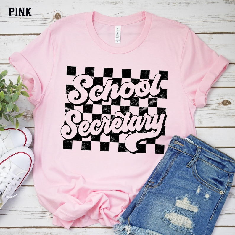 Peut inclure: T-shirt rose avec un fond &agrave; carreaux noir et blanc et le texte "School Secretary" dans une police r&eacute;tro.