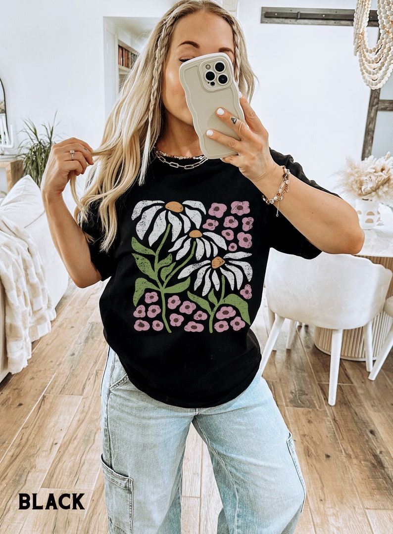 K&ouml;nnte beinhalten: Schwarzes T-Shirt mit einem grafischen Druck von wei&szlig;en G&auml;nsebl&uuml;mchen und rosa Blumen. Das Shirt ist oversized und hat eine lockere Passform.