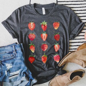 Op de afbeelding: Een donkergrijs T-shirt met een herhalend patroon van rode aquarel aardbeien. Het shirt is gemaakt van een zacht, comfortabel materiaal.