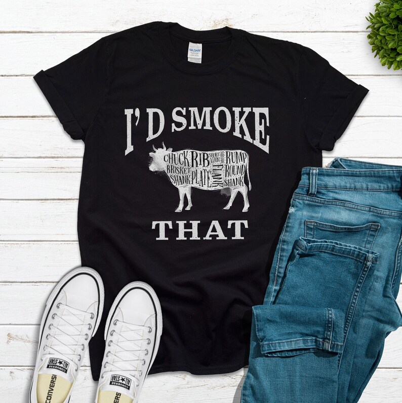 Puede incluir: Camiseta negra con un gr&aacute;fico blanco de una vaca con diferentes cortes de carne etiquetados. El texto "I'd Smoke That" est&aacute; debajo de la vaca.