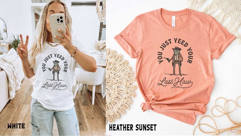 Puede incluir: Dos camisetas con una rana que lleva un sombrero de vaquero y sostiene una pistola. El texto en las camisetas dice "You just yeed your last haw". Las camisetas est&aacute;n disponibles en blanco y en color atardecer de brezo.