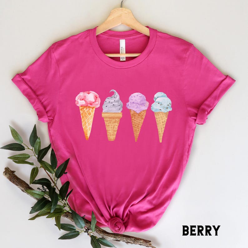 May include: Pink t-shirt with a graphic of four ice cream cones in different colors. The ice cream cones are watercolor painted and have a light pink, blue, purple, and green color scheme. The text "BERRY" is printed in white on the bottom right corner of the image.