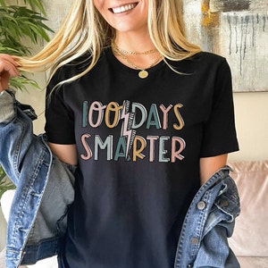 Pode incluir: Camiseta preta com o texto "100 Days Smarter" em letras coloridas com um gr&aacute;fico de raio.