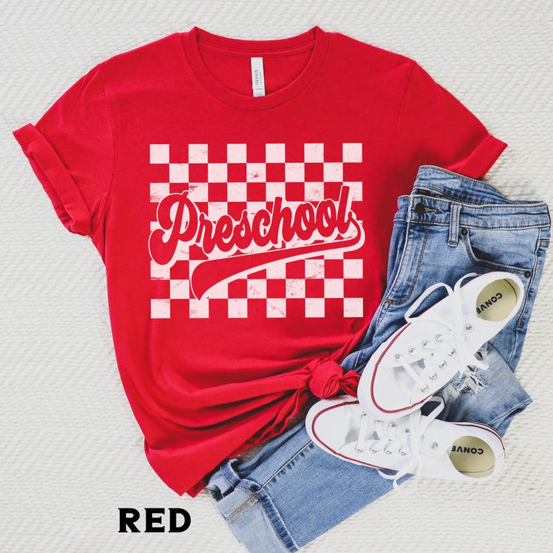 Pu&ograve; includere: T-shirt rosso con la scritta "Preschool" in un font retr&ograve; su un motivo a scacchi bianchi e rossi. La maglietta &egrave; abbinata a jeans blu e scarpe da ginnastica bianche.
