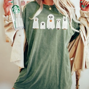 May include: A green t-shirt with a graphic of five dogs dressed as ghosts. The ghost dogs are wearing white sheets and have their heads poking out. One ghost dog is holding a small orange pumpkin.