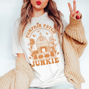 Könnte beinhalten: Ein weißes T-Shirt mit einer braunen Grafik eines Bauernhauses, Kürbissen und dem Text "Pumpkin Patch Junkie".